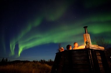 [Translate to Schwedisch:] Polarlicht am Himmel Gäste sitzen im Hotpot