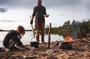 [Translate to Schwedisch:] Kind am Feuer mit dem Guide am kochen